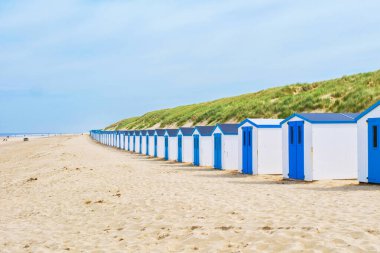 Teksas, Hollanda 'nın kumlu sahillerinde parlak güneşin altında bir sıra renkli plaj kulübesi duruyor..