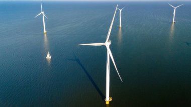 Hollanda 'da mavi gökyüzü yeşil enerji kavramına sahip elektrik üreten yel değirmeni türbinleri, off-shore yel değirmeni çiftliği, drone hava manzarası