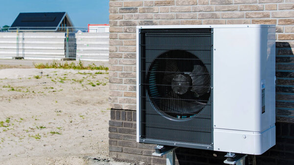 air source heat pump mounted on a building exterior in the Netherlands, complementing the backdrop of an active construction site under a bright blue sky. warmte pomp translation air source heat pump
