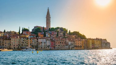Hırvatistan 'ın Rovinj kentinde güneş batarken, kıyı şeridi sıcak renklerle parlayarak, büyüleyici sahil binaları ve ikonik çan kulesini vurguluyor