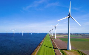 Bir sıra rüzgar türbini, Hollanda Flevoland 'da bahar zamanı sakin bir su kütlesinin yanında dimdik durur. Yel değirmeni türbinlerinin insansız hava görüntüsü okyanustaki yeşil enerjiyi