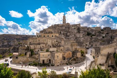 Tepelere yerleşen Matera İtalya çarpıcı taş binalarını ve dramatik bulutların ve mavi gökyüzünün altında dolambaçlı sokaklarını gözler önüne seriyor. Bu antik şehrin cazibesini ve tarihini tecrübe et..