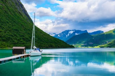 Beyaz bir yelkenli, Norveç fiyortlarının çarpıcı güzelliğiyle çevrili ahşap bir rıhtıma yanaştı. Bereketli yeşil tepeler Norangsfjorden Norangdal Urke Norveç 'in sakin ve berrak sularından yükseliyor.