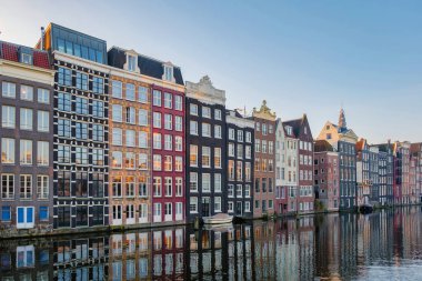 Sonbahar Amsterdam 'ı altın ve turuncu gölgelerle kaplarken şehrin ikonik kanal evleri sakin sularda parlıyor. Gün doğumunda Damrak Amsterdam