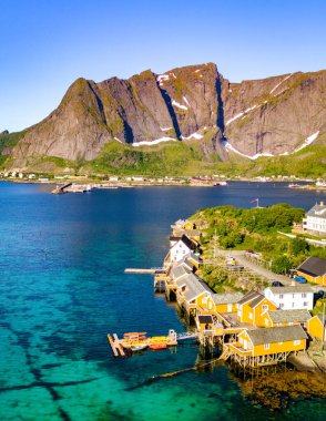 Fiyort 'un turkuaz suları boyunca renkli evlere sahip küçük Norveç köyü. Arka planda dağlar yükselir ve güzel bir zemin oluşturur. Sakrisoy, Lofoten, Norveç