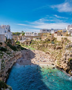 Polignano ve Karabasan Ziyaretçiler sıcak güneşin tadını çıkarırken Puglia 'nın sakin ve çarpıcı kıyı şeridinin tadını çıkarırken, kayalıklar yazın İtalya' da sakin mavi bir körfezi çerçeveliyor.