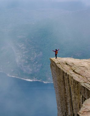 Bir yürüyüşçü, kolları açık bir uçurumun kenarında durur ve sisle kaplanmış Norveç fiyortlarının nefes kesici manzarasını seyreder. Norveç 'te daha önce yapılan yürüyüş