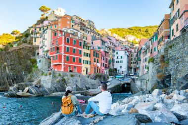 İki ziyaretçi, Cinque Terre 'deki Riomaggiore' un çarpıcı sahile karşı canlı binaların nefes kesici manzarasının keyfini çıkarıyorlar.