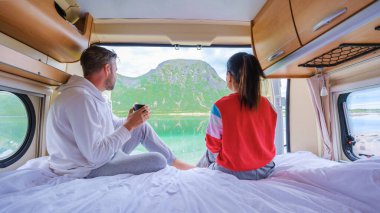 Bir çift, bir karavanda, bir karavanda, bir yatakta oturup kahvenin tadını çıkarırken, göz kamaştırıcı bir Norveç manzarasına bakıyorlar. Bir adam ve bir kadın, Lofoten Adaları Norveç 'teki bir karavanın penceresinden dışarı bakıyor.
