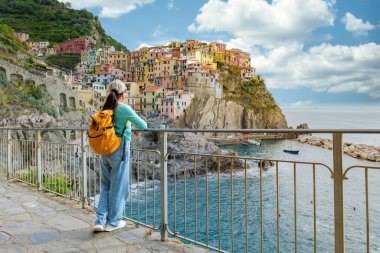 Cinque Terre 'nin uçurum kenarındaki köylerinin canlı renklerine hayran bir kadın gezgin, bulutlu bir gökyüzünün altında parıldıyor, Manarola İtalya sonbaharda