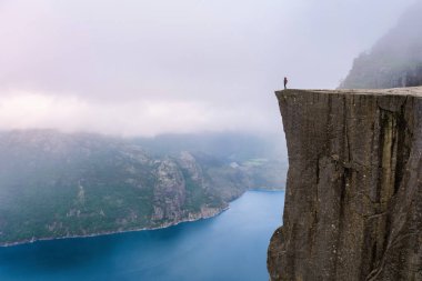 Preikestolen 'in kıyısında tek bir kişi duruyor, Norveç' in dramatik bir uçurumu, sisle kaplanmış engin bir su açıklığına bakıyor. Önceki bölümlerde, Norveç, tükenme veya büyüme başarısı kavramı 