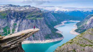 Norveç 'in Trolltunga kentinde yalnız bir yürüyüşçü duruyor. Norveç' in nefes kesici manzarasında sakin bir turkuaz göle bakan dramatik bir uçurum. Kadınlar dağın tepesinde