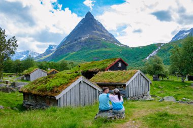 Yuvarlanan tepeler ve yüksek dağların arasına yerleşmiş yemyeşil çatıları olan geleneksel Norveç evlerinden oluşan bir küme. Norveç 'in iç kesimlerinde, çeşitli erkek ve kadınlar tatilde.