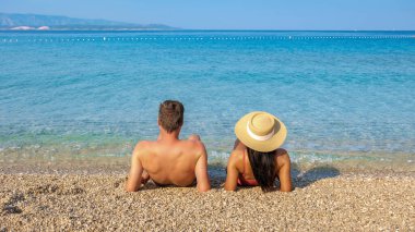 Brac Adası 'nın kumlu sahillerinde güneşlenen ve Hırvatistan' ın soluk soluğa kalmış Adriyatik Denizi 'nin nefes kesen manzarasının tadını çıkaran bir çift erkek ve kadın.