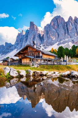 Yükselen Dolomite tepeleri, büyüleyici ahşap dağ evi dingin bir alp gölü, Dolomites Val Di Funes, İtalya Puez Odle Doğa Parkı 'ndaki Adolf Munkel Patikası' nda güzel bir şekilde yansıyor.