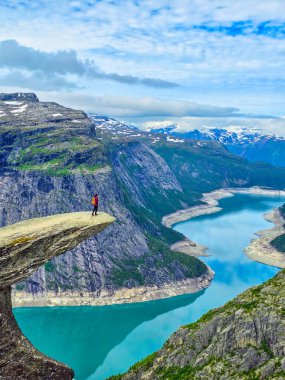 Soluk kesici bir uçurumun kenarında tek başına duran bir yürüyüşçü Norveç 'teki görkemli dağlarla çevrili bir fiyordun turkuaz sularına bakıyor. Trolltunga, Norveç Yazın