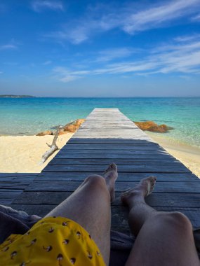 A peaceful moment spent lounging on a wooden pier, enjoying the serene turquoise waters and soft sand of Koh Munnork Island. Bright skies add to the idyllic atmosphere of this tropical paradise. clipart