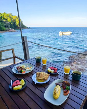 Koh Munnork Adası 'ndaki deniz kenarındaki bir masada taze meyve ve yerel yemeklerle nefis bir kahvaltı. Sakin okyanus manzarası mükemmel bir sabah atmosferi yaratır..