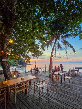Konuklar ahşap bir güvertede sallanan palmiyelerin altında güneş Koh Munnork Adası 'nın köpüklü sularının üzerinde batarken keyifli yemekler yiyip Tayland' da büyülü bir atmosfer yaratıyorlar..