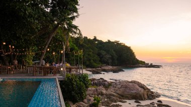 Alacakaranlık renkleri Koh Munnork Adası 'nı kaplıyor. Konuklar sakin sahilde akşamın tadını çıkarırken kıyı ışıkları altında parlıyor. Tayland' da dinlenmek için sakin bir atmosfer yaratıyor..