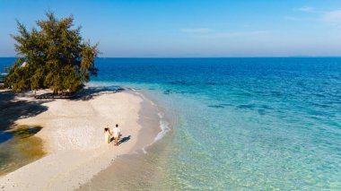 El değmemiş kumsalda gezinen iki kişi, Koh Munnork Adası 'nın huzurunun tadını çıkarıyor. Kristal berrak sular parlak mavi gökyüzünü yansıtıyor, Tayland 'da güzel bir an yaratıyor.