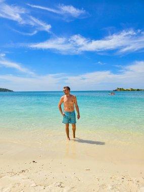 Samae San Adası 'nın yumuşak kumlarında duran bir adam sıcak güneşin ve sakin dalgaların tadını çıkarıyor. Çarpıcı mavi gökyüzü ve turkuaz su Tayland 'da mükemmel bir tropik cennet yaratır..