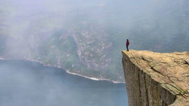Yalnız bir yürüyüşçü, sis ve sakin fiyortlarla çevrili Preikestolen 'in kıyısından nefes kesici manzaralardan hoşlanır. Lysefjorden Norveç