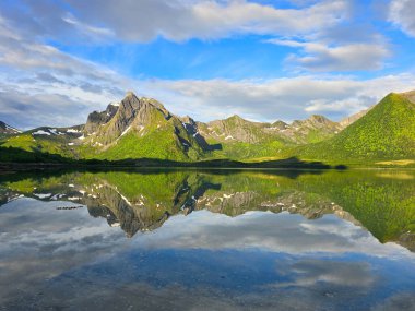 Nefes kesen yeşil dağlar görkemli bir şekilde yükselir. Titreyen gökyüzünün altındaki sakin bir gölde mükemmel bir şekilde yansıtılır..