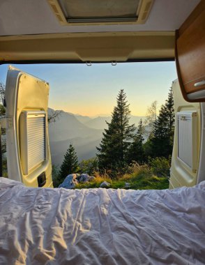 Avusturya Hallstatt 'ü çevreleyen görkemli dağları aydınlatan şafağın yumuşak ışığına uyanmak. Dağların üzerinde güzel manzarası olan rahat bir karavanda dinleniyorum.
