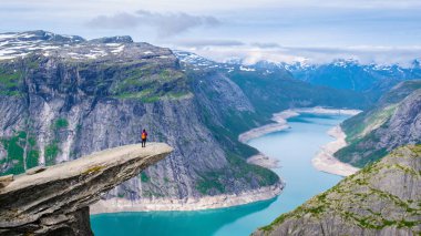 Norveç 'teki Trolltunga uçurumunun kenarında duran yalnız bir kadın yürüyüşçü geniş, mavi bir fiyorda bakıyor. Norveç, Trolltunga 'da Asyalı kadınlar. Dağın tepesinde bir kadın