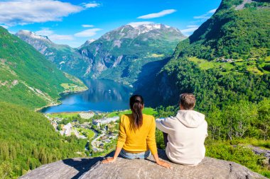 Bir çift yeşil dağlarla çevrili, göz kamaştırıcı bir Norveç fiyorduna tepeden bakan kayalıklarda oturuyor. Geiranger Fjord Norveç 'te çeşitli kadın ve erkekler var.