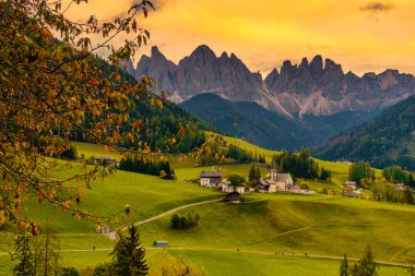 Yuvarlanan yeşil tepeler görkemli Dolomitlere karışıp nefes kesici bir zemin oluşturuyor. Tuhaf köyler manzarayı süslüyor, Santa Maddalena Val di Funes İtalya sonbahar sezonu