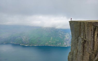 Bir yürüyüşçü uçurumun kenarında duruyor ve sisle kaplanmış Norveç fiyortlarının nefes kesici manzarasını seyrediyor. Norveç, Preikestolen