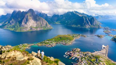 Norveç 'te bir dağın tepesinde duran iki kişi fiyortların ve adaların çarpıcı manzarasına hayran kaldılar. Reinebringen Dağı, Lofoten, Norveç 'te yürüyüş yapan birkaç erkek ve kadın.