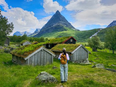Bir gezgin Norveç 'in bereketli iç kesimlerindeki Norveç' in yüksek bir dağının altındaki büyüleyici çim çatılı evlere doğru ilerliyor.