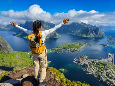 Neşeli bir maceracı Norveç 'teki Lofoten Adaları' nın dağlarla ve sakin sularla çevrili nefes kesici manzarasını kucaklıyor. Dağın tepesinde elleri havada Asyalı kadınlar.