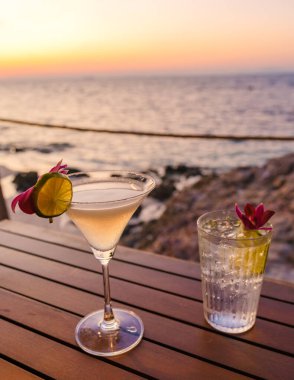 Relaxation takes center stage as refreshing cocktails are savored on a wooden table, framed by the breathtaking sunset over Koh Munnork Island Thailand. clipart