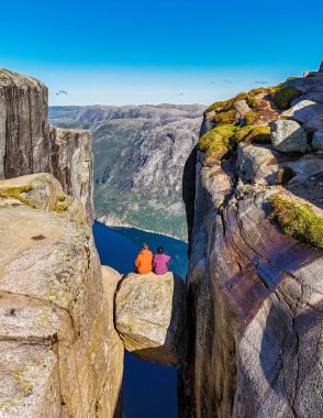 Norveç 'teki derin bir vadiye bakan dar bir kaya çıkıntısında iki kişi oturuyor. Muhteşem Kjeragbolten uçurumu Yazın Kjeragbolten 'daki bu cesur çift için nefes kesici bir zemin hazırlıyor.