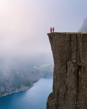 Norveç 'teki Preikestolen uçurumundan nefes kesici bir manzara. Uçsuz bucaksız araziye bakan iki figürle birlikte. Yazın Norveç 'te yürüyüş yapan bir çift erkek ve kadın.