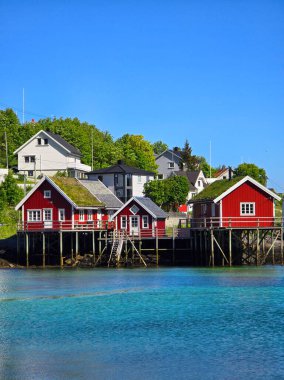 Reine, Lofoten, Norway,A group of traditional red houses with grass roofs stand on stilts in the crystal clear water of a Norwegian fjord at the Lofoten Islands clipart