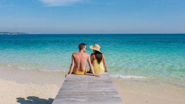 Birlikte ahşap bir rıhtımda oturan bir çift Tayland 'ın Rayong kentindeki Koh Munnork Adası' nın nefes kesici manzarasının tadını çıkarıyor. Sakin turkuaz sular ve parlak güneş mükemmel bir tropikal kaçış yaratır..