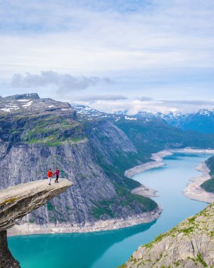 Norveç, Trolltunga 'da bir çift, Norveç' te manzaralı bir fiyorda bakan bir uçurumun kenarında duruyor. Erkekler ve kadınlar yazın Norveç, Trolltunga 'da bir dağın tepesinde.