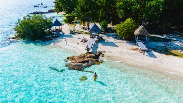 Tayland 'ın Rayong kentindeki Koh Munnork Adası' nın berrak turkuaz sularının rahatlamaya yol açtığı huzurlu güzelliğini keşfedin. Kumsaldaki bir çiftin drone görüntüsü.