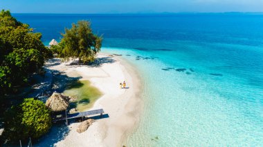 Yumuşak kumlar ve berrak sular Koh Munnork Adası Tayland 'da pitoresk bir ortam yaratır. İki ziyaretçi, sıcak güneşin altında okyanusun canlı renklerinde, kıyı boyunca yürürler..