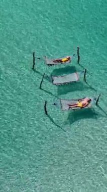 Çeşitli bir çift, Tayland 'daki Koh Kood Adası' nın çarpıcı turkuaz okyanus suları üzerinde asılı dururken hamaklarda huzurlu bir öğleden sonranın tadını çıkarıyor. Mükemmel bir tropikal kaçış.