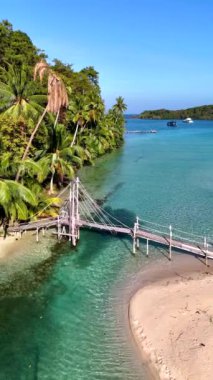 Tayland 'daki Koh Kood Adası' nın dingin cazibesini keşfedin. İçinde el değmemiş sular, kumlu plajlar, sallanan palmiye ağaçları ve kumsalın üzerinde eski ahşap bir köprü vardır.