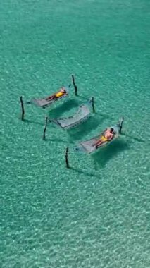 Koh Kood Adası 'nın dingin güzelliğinin tadını çıkarın. Etrafı çarpıcı turkuaz sular ve serin bir okyanus esintisiyle çevrili iki insan hamaklarda dinleniyor. Tayland 'da çeşitli kadın ve erkekler var.