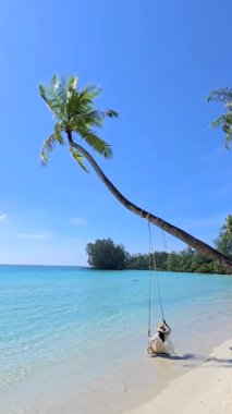 Koh Kood, Tayland 'ın sakinliğinde bir salıncak kristal berrak suların yanındaki yüksek bir palmiye ağacından sarkıyor. Bir kadın salıncakta sallanıyor palmiye ağacının altında