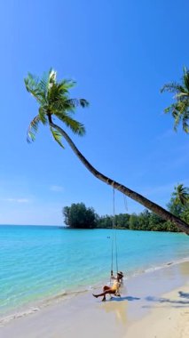 Tayland, Koh Kood 'un huzurlu güzelliğini hissedin. Huzurlu bir salıncak bir palmiye ağacından sarkıyor. Çarpıcı turkuaz suların tadını çıkar. Palmiye ağacının altında sallanan bir kadın.