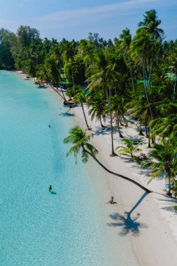 Sersemletici panoramik manzara, kristal berraklığında suların bereketli palmiye ağaçlarıyla çevrili yumuşak beyaz kumda hafifçe yuvarlandığını gösteriyor. Ziyaretçiler güneşli bir günde Koh Kood 'un huzurlu güzelliğinin tadını çıkarıyorlar..